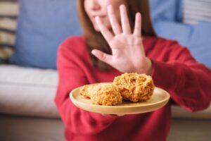 Closeup of a woman making hand sign to refuse fried chicken for | Aaria Rheumatology avoid foods