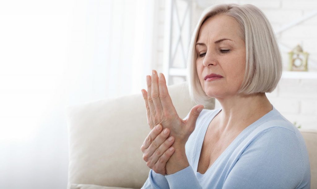 Woman stretching her stiff fingers in the morning — early arthritis awareness.